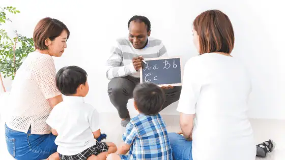 A male teacher supporting children with their mums to learn the English alphabet