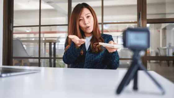 A woman sat in a suit at a desk in front of a camera.