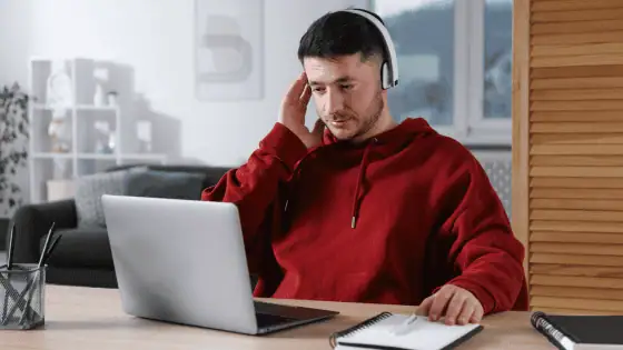 man with headset sat in front of laptop taking notes