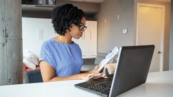 woman sat in front of laptop holding book appearing to be studying